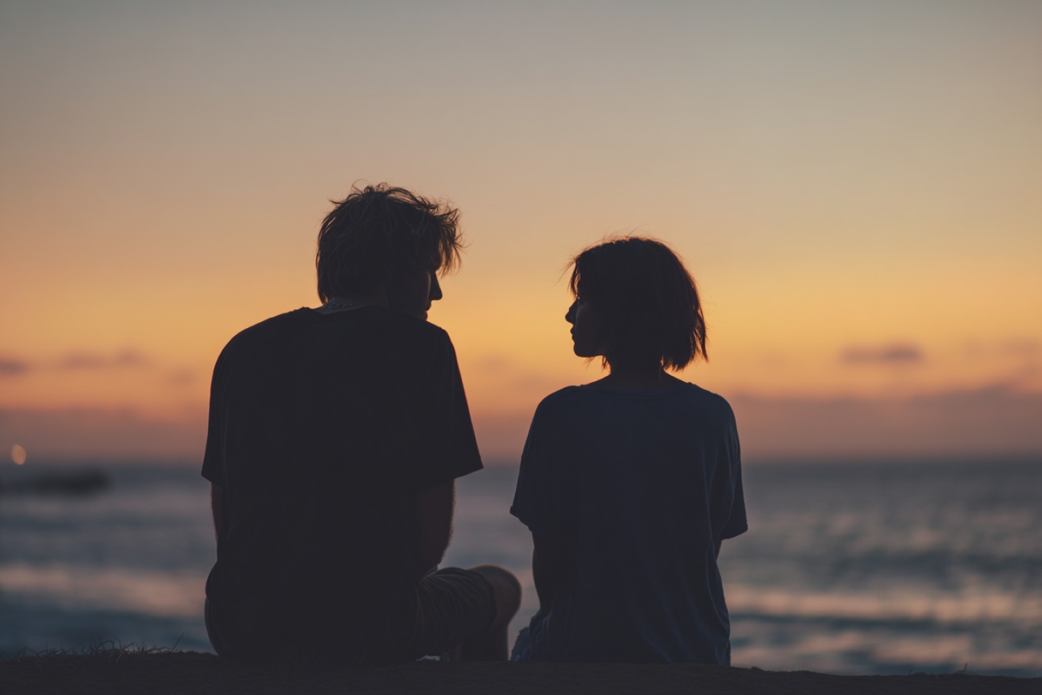 Two people sitting together at sunset near the water, reflecting and seeking comfort often supported through Summit, NJ cremation services.